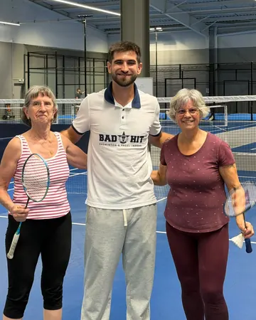 Un membre de l’équipe entouré de deux joueuses, raquettes de badminton en main