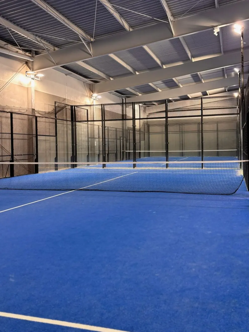 Terrain de padel couvert de Bad Hit, au sol bleu, vu depuis le fond du court