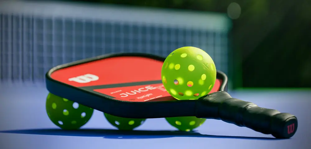 Raquette et balles de pickleball posées sur un terrain